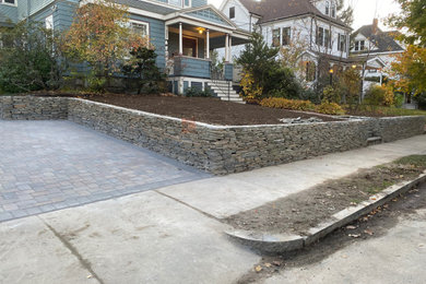Photo of a large front yard driveway in Boston with a retaining wall and concrete pavers.