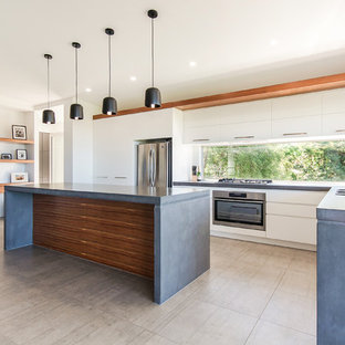 This is an example of a mid-sized modern kitchen pantry in Sunshine Coast with a farmhouse sink, white cabinets, concrete benchtops, window splashback, stainless steel appliances, porcelain floors, with island and beige floor.