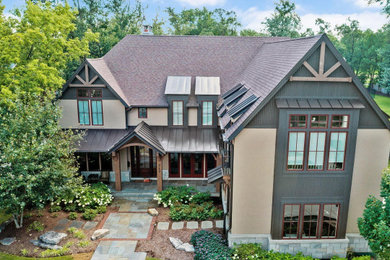 Diseño de fachada de casa beige y marrón rural grande de tres plantas con revestimiento de estuco, tejado a dos aguas, tejado de teja de madera y panel y listón