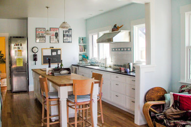 Eat-in kitchen - mid-sized craftsman single-wall medium tone wood floor eat-in kitchen idea in San Francisco with a double-bowl sink, flat-panel cabinets, white cabinets, soapstone countertops, white backsplash, ceramic backsplash, stainless steel appliances and an island