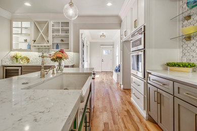 Eat-in kitchen - mid-sized modern galley light wood floor and brown floor eat-in kitchen idea in Toronto with a farmhouse sink, recessed-panel cabinets, white cabinets, quartz countertops, white backsplash, ceramic backsplash, stainless steel appliances, an island and white countertops