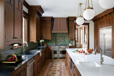 Arts and crafts u-shaped medium tone wood floor and brown floor kitchen photo in Nashville with an undermount sink, shaker cabinets, medium tone wood cabinets, green backsplash, stainless steel appliances, an island and black countertops