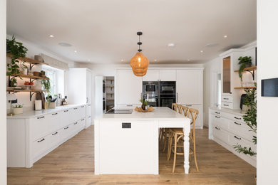 Design ideas for a large nautical open plan kitchen in Other with a built-in sink, shaker cabinets, white cabinets, quartz worktops, black appliances, ceramic flooring, an island, brown floors and white worktops.