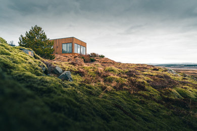 Inspiration for a small contemporary brown one-story wood and clapboard exterior home remodel in Other with a mixed material roof and a black roof