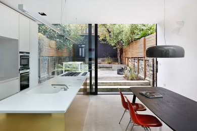 Photo of a large modern galley kitchen/diner in London with a built-in sink, flat-panel cabinets, white cabinets, stainless steel appliances, concrete flooring, an island and grey floors.