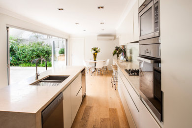Design ideas for a mid-sized contemporary single-wall eat-in kitchen in Sydney with a double-bowl sink, flat-panel cabinets, white cabinets, marble benchtops, white splashback, glass sheet splashback, stainless steel appliances, light hardwood floors and with island.
