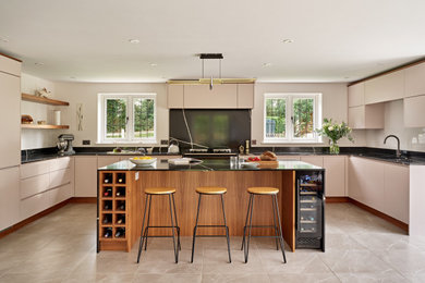 Photo of a large modern u-shaped open plan kitchen in Buckinghamshire with a built-in sink, flat-panel cabinets, pink cabinets, engineered stone countertops, black splashback, engineered quartz splashback, black appliances, an island, black worktops and feature lighting.