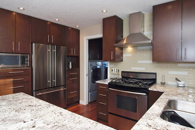 Mid-sized contemporary u-shaped eat-in kitchen in Calgary with a double-bowl sink, flat-panel cabinets, dark wood cabinets, granite benchtops, beige splashback, glass tile splashback, stainless steel appliances, medium hardwood floors and a peninsula.