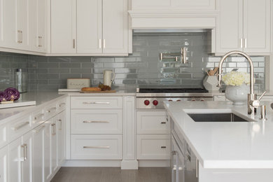 This is an example of a large transitional l-shaped open plan kitchen in New York with an undermount sink, shaker cabinets, white cabinets, quartz benchtops, grey splashback, ceramic splashback, stainless steel appliances, porcelain floors, with island, beige floor and beige benchtop.