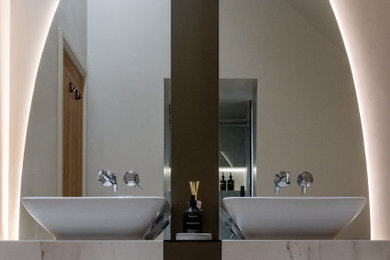 This is an example of a large contemporary ensuite bathroom in West Midlands with flat-panel cabinets, brown cabinets, a built-in bath, a built-in shower, a wall mounted toilet, beige tiles, porcelain tiles, beige walls, porcelain flooring, a vessel sink, tiled worktops, beige floors, a sliding door, beige worktops, feature lighting, double sinks, a floating vanity unit and a vaulted ceiling.