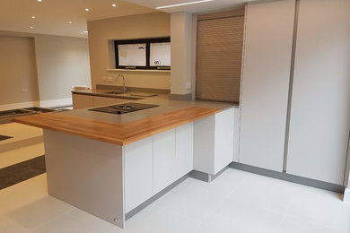 This is an example of a large modern open plan kitchen in London with a built-in sink, flat-panel cabinets, quartz worktops, stainless steel appliances, porcelain flooring and a breakfast bar.