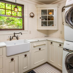 Photo of a small rural l-shaped separated utility room in Other with a belfast sink, recessed-panel cabinets, beige cabinets, marble worktops, beige walls, ceramic flooring, a stacked washer and dryer and pink floors.