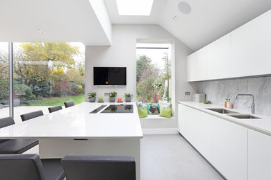 Photo of a contemporary kitchen in London with a double-bowl sink, flat-panel cabinets, white cabinets, grey splashback, a peninsula, grey floor and white benchtop.