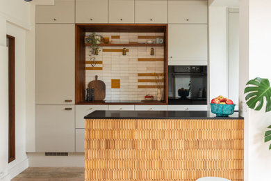 Photo of an eclectic u-shaped kitchen in London with flat-panel cabinets, multi-coloured splashback, black appliances, medium hardwood flooring, a breakfast bar, brown floors, black worktops and beige cabinets.