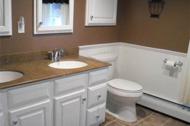This is an example of a mid-sized traditional 3/4 bathroom in Bridgeport with raised-panel cabinets, white cabinets, an alcove tub, a shower/bathtub combo, a two-piece toilet, beige tile, stone tile, brown walls, porcelain floors, an undermount sink and solid surface benchtops.