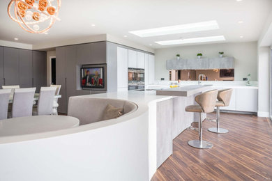 This is an example of a large contemporary open plan kitchen in Kent with white cabinets, quartzite benchtops, grey splashback, mirror splashback, with island and white benchtop.