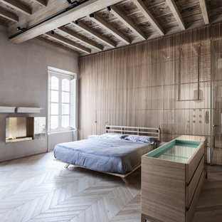 Cette photo montre une grande chambre parentale tendance avec un mur gris, un sol en bois clair, cheminée suspendue et un manteau de cheminée en pierre.