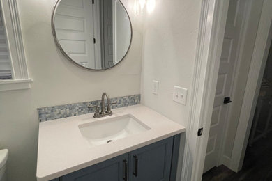 Example of a beach style kids' blue tile and glass sheet slate floor, black floor and single-sink bathroom design with shaker cabinets, blue cabinets, gray walls, an undermount sink, quartzite countertops, a hinged shower door, white countertops and a built-in vanity