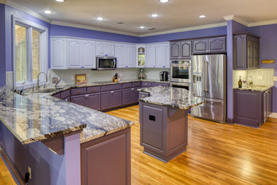Example of a mid-sized trendy medium tone wood floor and brown floor kitchen design in Atlanta with a single-bowl sink, raised-panel cabinets, purple cabinets, granite countertops, gray backsplash, glass tile backsplash, stainless steel appliances, an island and black countertops