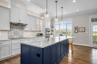 Eat-in kitchen - transitional l-shaped medium tone wood floor and brown floor eat-in kitchen idea in DC Metro with a farmhouse sink, shaker cabinets, white cabinets, quartz countertops, white backsplash, ceramic backsplash, stainless steel appliances, an island and gray countertops