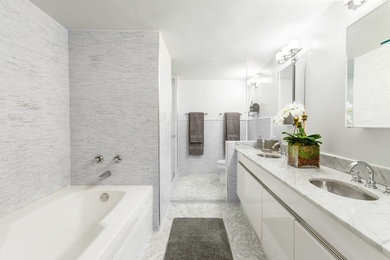 Photo of a large contemporary master bathroom in New York with flat-panel cabinets, white cabinets, gray tile, mosaic tile, marble floors, marble benchtops, a drop-in tub, white walls and an undermount sink.