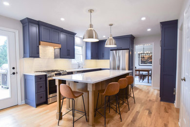Inspiration for a mid-sized transitional l-shaped light wood floor enclosed kitchen remodel in Other with an undermount sink, shaker cabinets, blue cabinets, quartz countertops, white backsplash, ceramic backsplash, stainless steel appliances, an island and white countertops