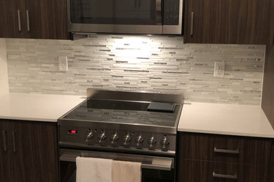 Design ideas for a mid-sized modern galley separate kitchen in Toronto with flat-panel cabinets, dark wood cabinets, solid surface benchtops, white splashback, glass tile splashback, stainless steel appliances and white benchtop.