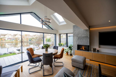 This is an example of a medium sized contemporary grey and white open plan living room in Gloucestershire with medium hardwood flooring, a stone fireplace surround, a wall mounted tv, a vaulted ceiling and feature lighting.
