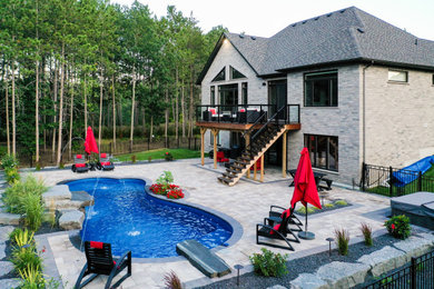 Large country backyard custom-shaped pool in Toronto with concrete pavers.
