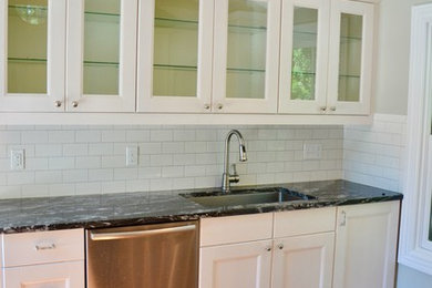 Small transitional medium tone wood floor enclosed kitchen photo with an undermount sink, glass-front cabinets, granite countertops, white backsplash, ceramic backsplash and stainless steel appliances
