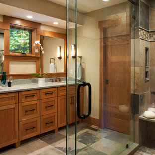 Cette photo montre une grande salle de bain principale craftsman avec un placard à porte shaker, des portes de placard en bois brun, une douche d'angle, un carrelage multicolore, un carrelage de pierre, un mur beige, un sol en ardoise, un lavabo encastré et un plan de toilette en granite.