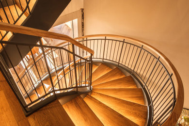 This is an example of an expansive contemporary wood curved metal railing staircase spindle in Cambridgeshire with metal risers.