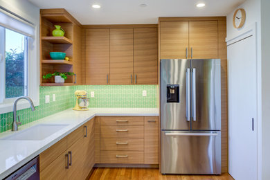 Foto på ett mellanstort vit l-kök, med en undermonterad diskho, släta luckor, skåp i ljust trä, grönt stänkskydd, stänkskydd i keramik, rostfria vitvaror, ljust trägolv och brunt golv