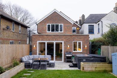 This is an example of a medium sized midcentury two floor brick and rear house exterior in London with a pitched roof, a tiled roof and a red roof.