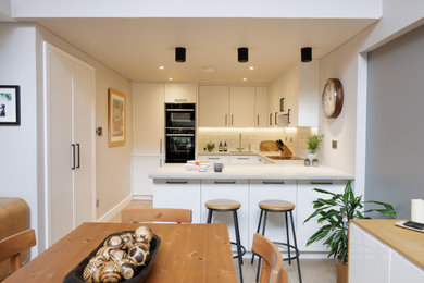 Photo of a modern kitchen in London with a single-bowl sink, shaker cabinets, white cabinets, concrete worktops, white splashback, metro tiled splashback, integrated appliances and grey worktops.