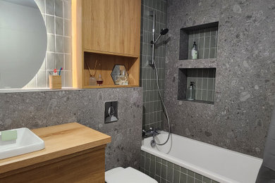 Exemple d'une petite salle de bain principale et blanche et bois tendance en bois clair avec un placard à porte affleurante, une baignoire encastrée, WC suspendus, un carrelage vert, des carreaux de céramique, un mur gris, un sol en carrelage de céramique, un lavabo posé, un plan de toilette en bois, un sol gris, un plan de toilette marron, du carrelage bicolore, meuble simple vasque et meuble-lavabo encastré.