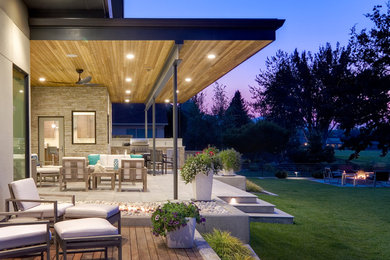 This is an example of a mid-sized modern backyard patio in Seattle with an outdoor kitchen, natural stone pavers and a roof extension.