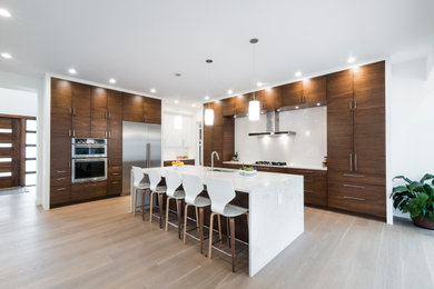 This is an example of a large contemporary l-shaped open plan kitchen in Detroit with a single-bowl sink, flat-panel cabinets, medium wood cabinets, quartz benchtops, white splashback, porcelain splashback, stainless steel appliances, light hardwood floors, with island, beige floor and white benchtop.