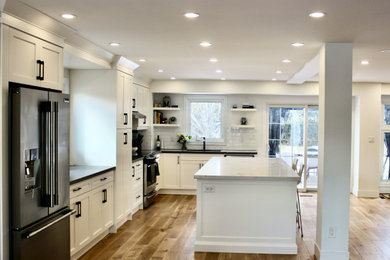 Large trendy l-shaped medium tone wood floor and brown floor eat-in kitchen photo in Toronto with an undermount sink, shaker cabinets, white cabinets, quartz countertops, white backsplash, porcelain backsplash, stainless steel appliances, an island and white countertops