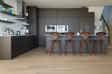 Large minimalist l-shaped light wood floor eat-in kitchen photo in Ottawa with flat-panel cabinets, dark wood cabinets, quartz countertops, white backsplash, ceramic backsplash, stainless steel appliances and an island