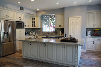 Inspiration for a timeless l-shaped kitchen remodel in Orange County with raised-panel cabinets, white cabinets, quartzite countertops, stone slab backsplash, stainless steel appliances and an island