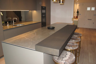 This is an example of a large modern galley open plan kitchen in London with an integrated sink, recessed-panel cabinets, grey cabinets, tile countertops, grey splashback, glass tiled splashback, coloured appliances, porcelain flooring, an island, brown floors, green worktops and a coffered ceiling.