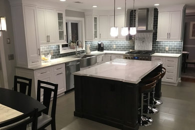 Mid-sized transitional l-shaped porcelain tile and gray floor kitchen photo in New York with a farmhouse sink, beaded inset cabinets, white cabinets, quartzite countertops, gray backsplash, subway tile backsplash, stainless steel appliances, an island and white countertops
