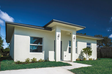 Small trendy white one-story stucco house exterior photo in Miami with a hip roof, a shingle roof and a black roof