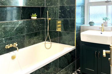 Small contemporary shower room bathroom in London with freestanding cabinets, green cabinets, a built-in bath, a shower/bath combination, a wall mounted toilet, marble tiles, a console sink, a shower curtain, white worktops, a single sink, a built in vanity unit, white walls, ceramic flooring and black floors.