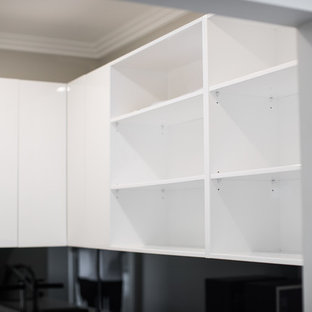 Inredning av ett modernt stort kök, med en köksö, släta luckor, vita skåp, bänkskiva i kvarts, svart stänkskydd, glaspanel som stänkskydd, rostfria vitvaror, en nedsänkt diskho, plywoodgolv och grått golv