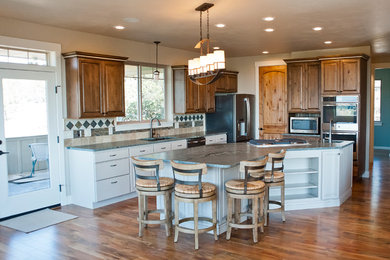 Example of a large mountain style u-shaped medium tone wood floor and brown floor eat-in kitchen design in Other with an undermount sink, raised-panel cabinets, medium tone wood cabinets, limestone countertops, green backsplash, ceramic backsplash, stainless steel appliances, an island and green countertops