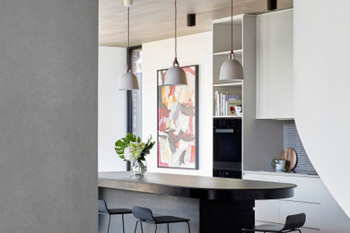 Inspiration for a mid-sized contemporary galley eat-in kitchen in Melbourne with a drop-in sink, flat-panel cabinets, white cabinets, solid surface benchtops, blue splashback, ceramic splashback, black appliances, concrete floors, with island, grey floor and black benchtop.