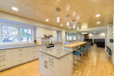 Open concept kitchen - mid-sized modern u-shaped light wood floor and beige floor open concept kitchen idea in Calgary with an undermount sink, flat-panel cabinets, white cabinets, solid surface countertops, gray backsplash, ceramic backsplash, stainless steel appliances and an island