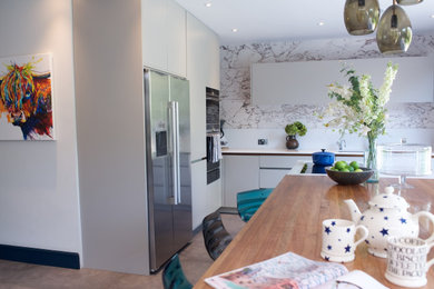 Inspiration for a large contemporary l-shaped ceramic tile and gray floor open concept kitchen remodel in London with a double-bowl sink, flat-panel cabinets, gray cabinets, wood countertops, white backsplash, quartz backsplash, stainless steel appliances, an island and white countertops